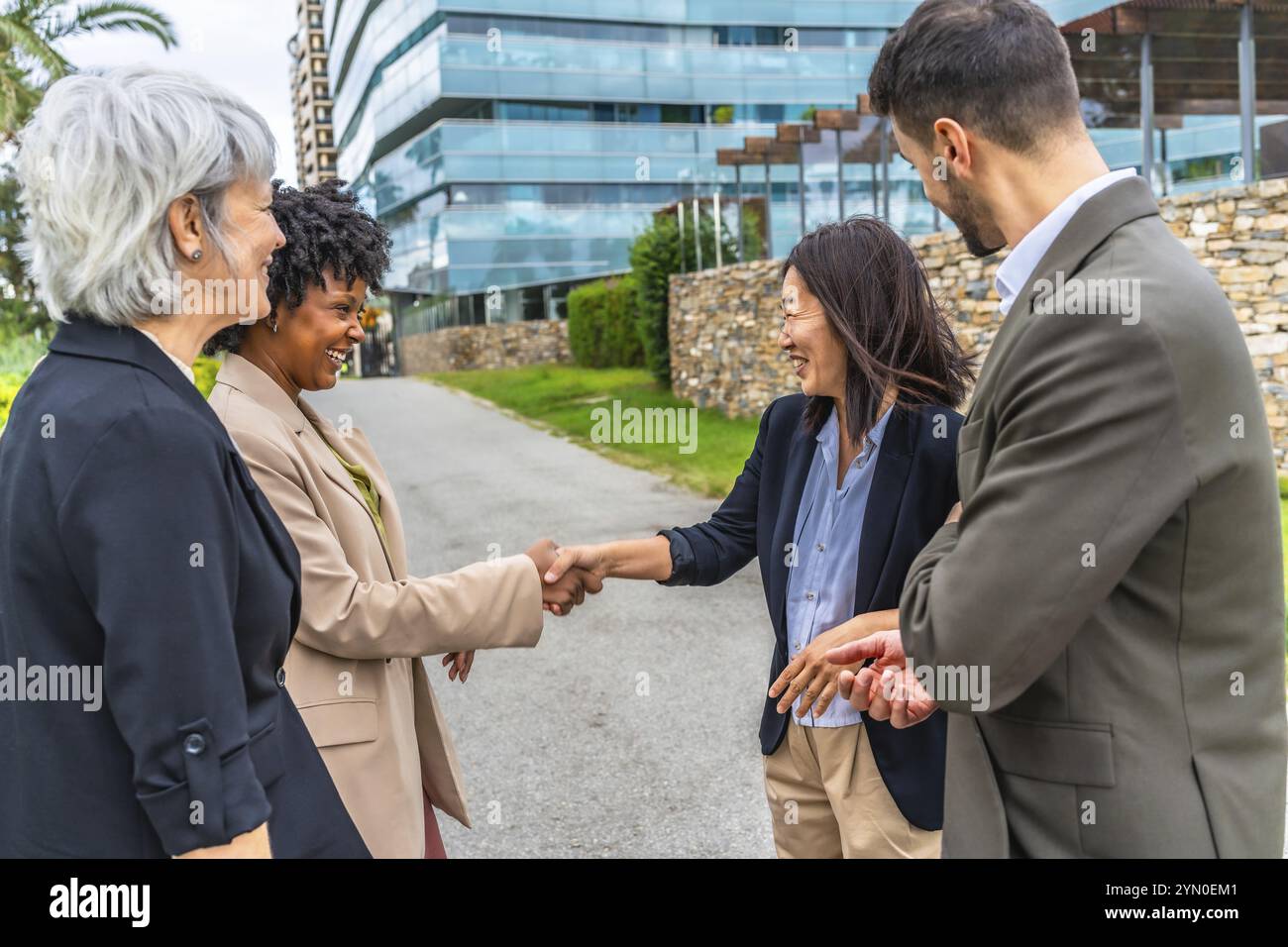 Des femmes d'affaires multiethniques se serrant la main lors d'une réunion en plein air à côté de collègues d'affaires dans la ville Banque D'Images