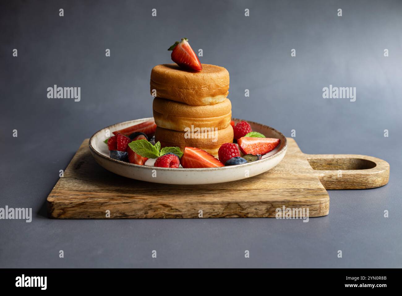 Pile de crêpes japonaises moelleuses servies avec des fraises fraîches, des framboises, des bleuets et des feuilles de menthe sur une planche de bois rustique et une assiette en céramique Banque D'Images