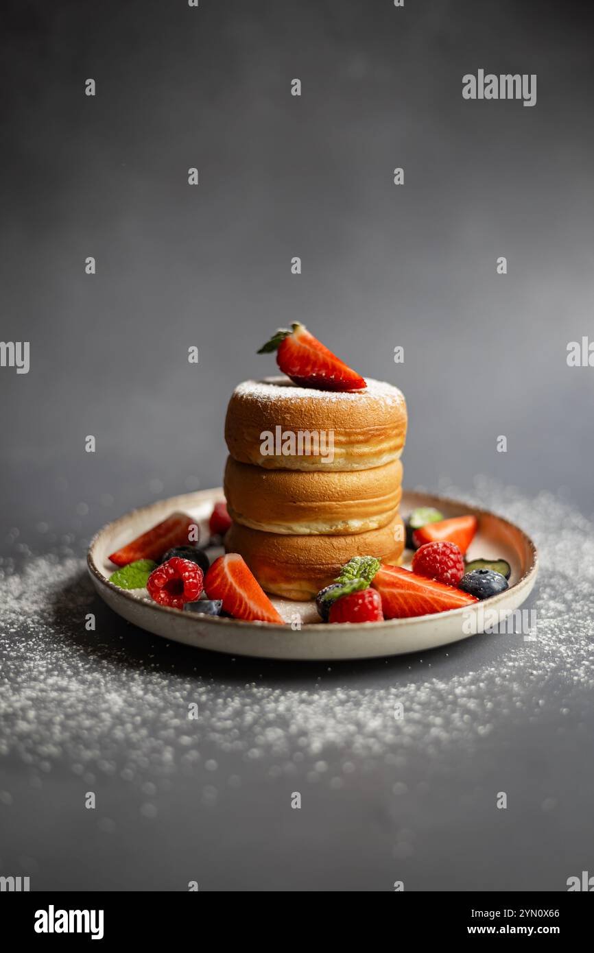 Pile de crêpes japonaises moelleuses servies avec des fraises fraîches, des framboises, des bleuets et un saupoudrage de sucre en poudre sur une assiette en céramique Banque D'Images