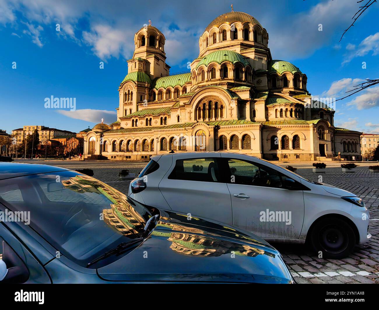 Réflexions de la foi : voitures garées devant la cathédrale Alexandre Nevsky. Sofia Bulgarie 2024. Ciel bleu avec des nuages. Banque D'Images