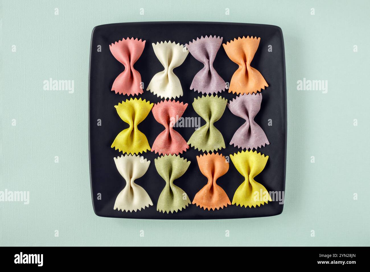 Grandes pâtes Farfalle colorées disposées sur une assiette carrée noire Banque D'Images