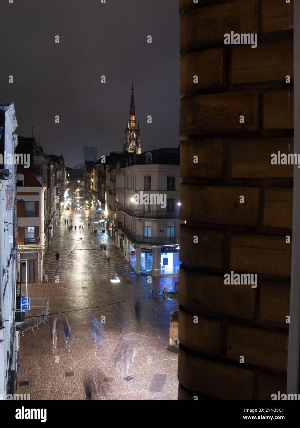 Regardant de derrière un mur des gens flous sous la pluie, illuminés par l'éclairage public en début de soirée, Rue de sec Arembault, Lille Banque D'Images