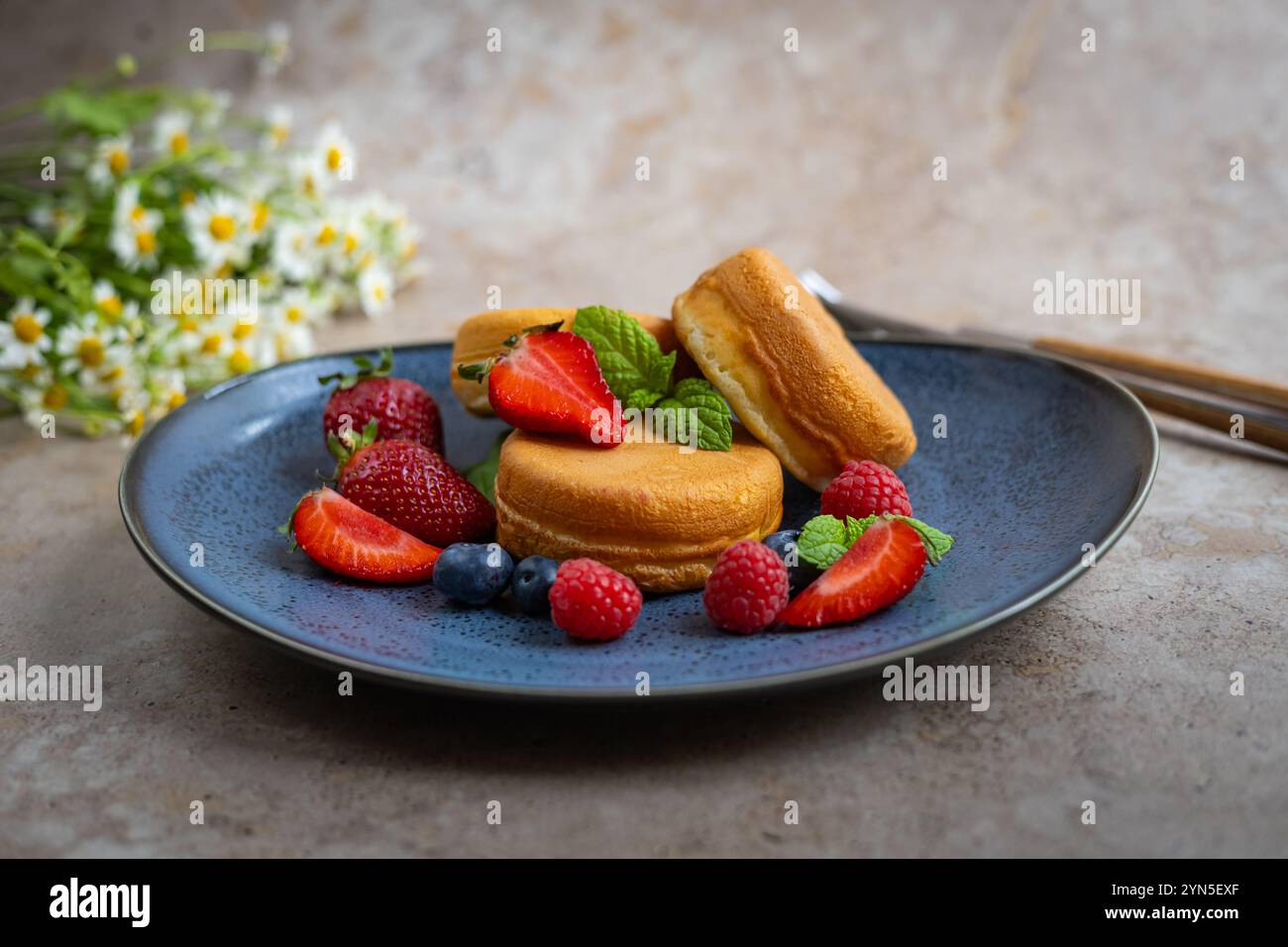 Crêpes gourmandes servies sur une élégante assiette bleue avec des baies fraîches et des feuilles de menthe. Petit déjeuner élégant, dessert d'été et nourriture naturelle Banque D'Images