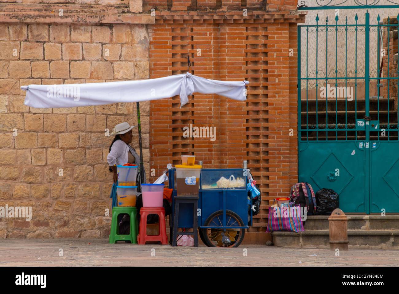 Un vendeur ambulant avec un chariot mobile et des fournitures colorées se tient devant un mur de briques à sucre, en Bolivie. Banque D'Images