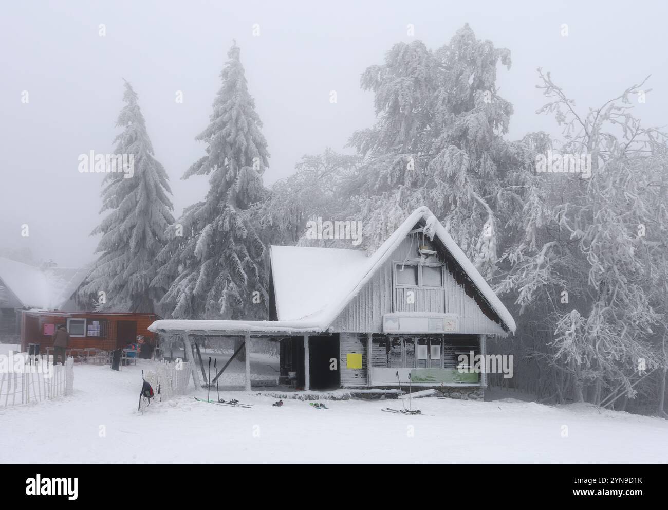 Paysage d'hiver fantastique avec maison en bois lumineux sur fond de lumières de ville dans le brouillard. Chalet confortable dans les montagnes Carpathian. Noël Banque D'Images