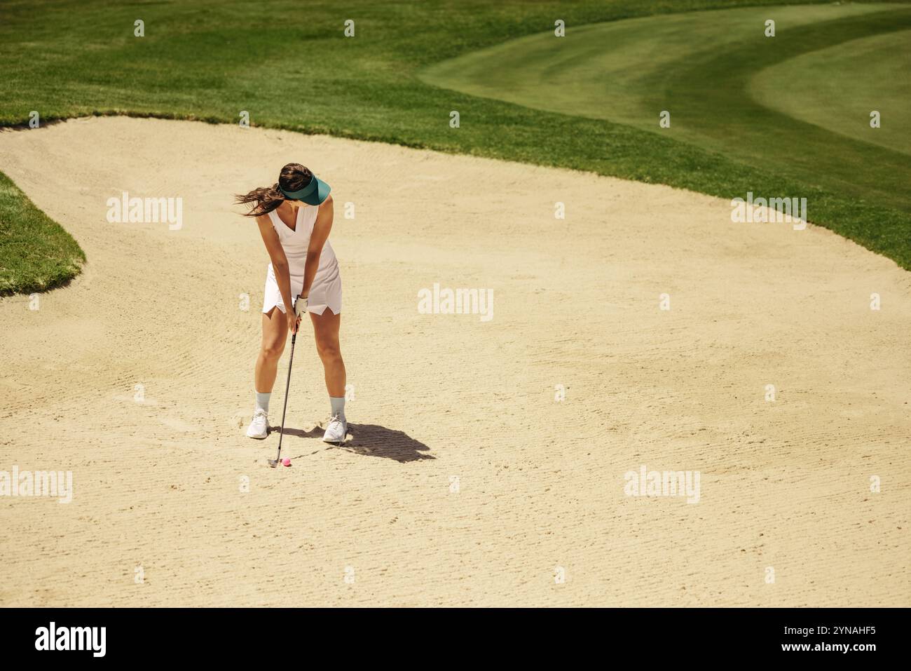 Golfeuse dans le bunker de sable visant et se préparant à prendre un coup de feu. Elle maintient une position concentrée comme elle se concentre sur frapper la balle de golf. Banque D'Images
