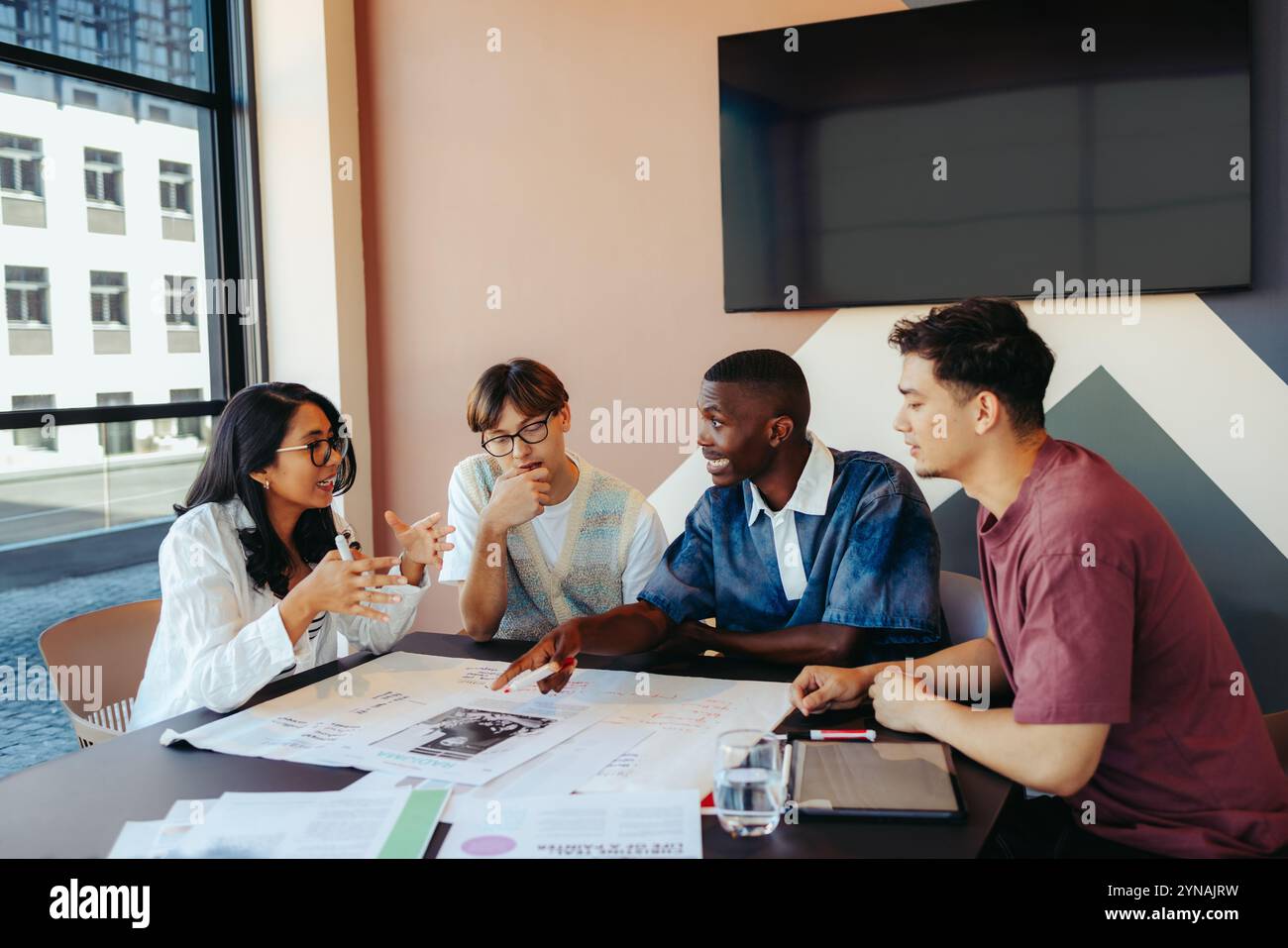 Un groupe d'étude diversifié dans une discussion intense, collaborant sur des notes et une tablette dans un cadre moderne. Étudiants engagés travaillant ensemble. Banque D'Images