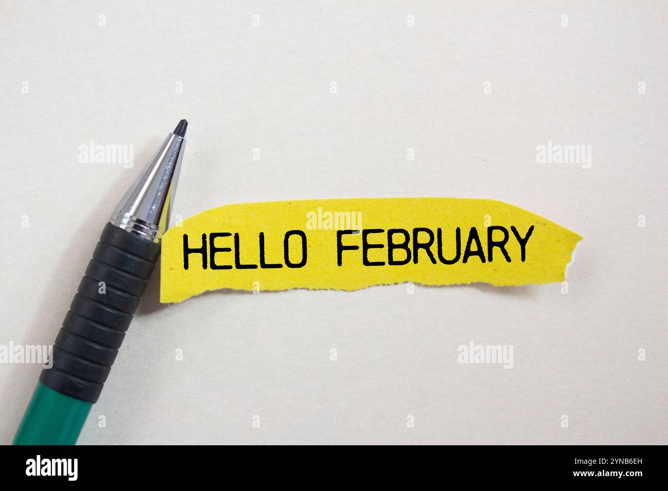 Bonjour février message écrit sur un morceau de papier jaune déchiré déchiré et un stylo avec fond blanc. Symbole conceptuel bonjour février. Copier l'espace. Banque D'Images