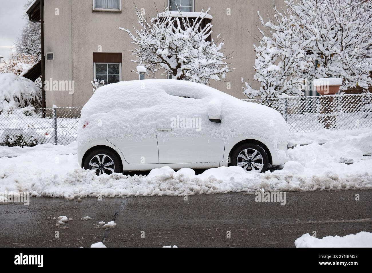 Petite voiture blanche à hayon recouverte de neige garée dans la rue après de fortes chutes de neige. Gros plan vue grand angle, pas de gens. Banque D'Images