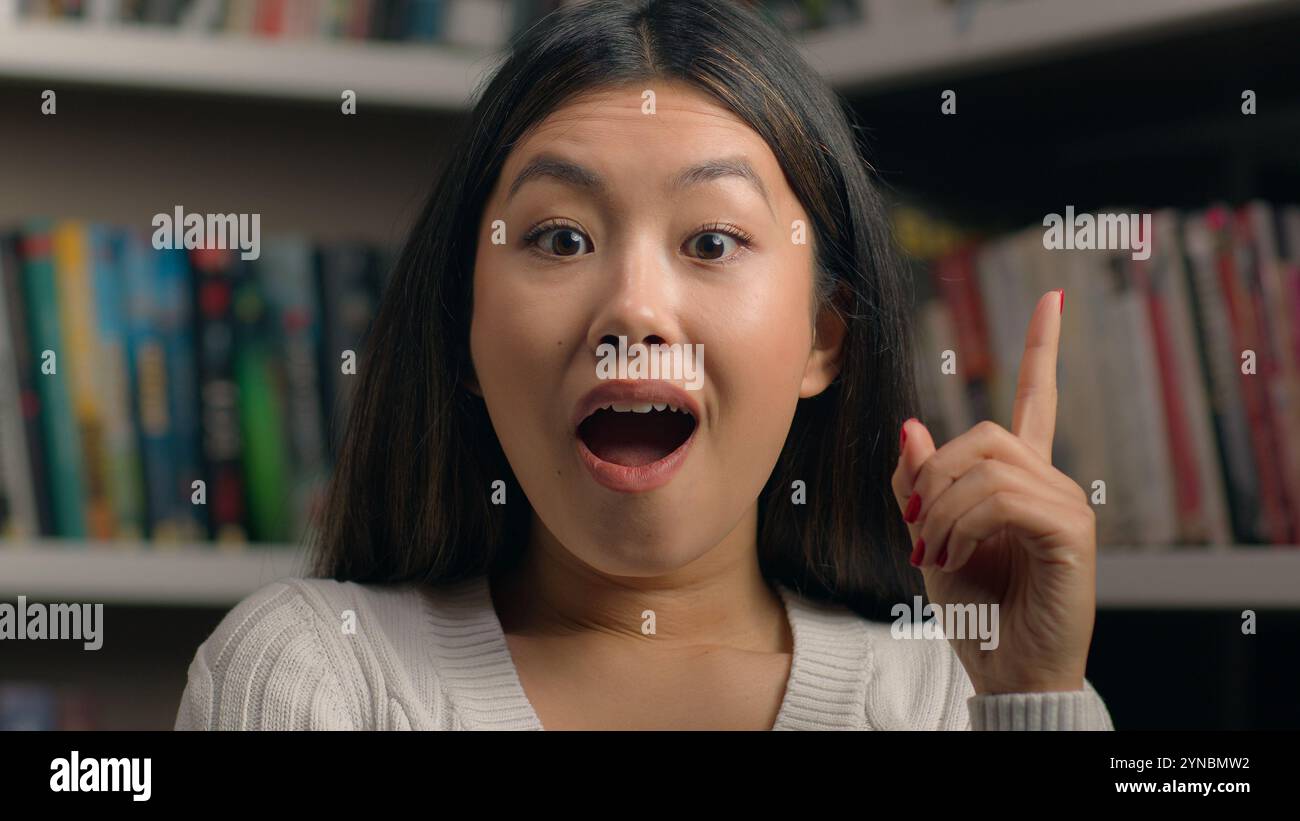 Portrait féminin souriant femme asiatique heureuse étudiante de 20 ans regardant la caméra dans la bibliothèque de l'université montrant les pouces vers le haut comme le symbole d'approbation de geste Banque D'Images