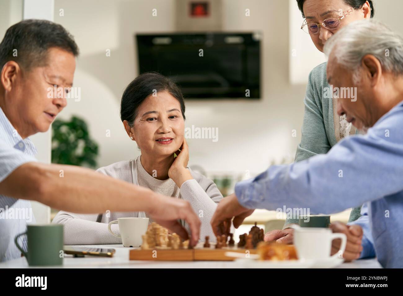 groupe de personnes âgées asiatiques heureuses deux couples se réunissant à la maison jouant le jeu d'échecs ensemble Banque D'Images