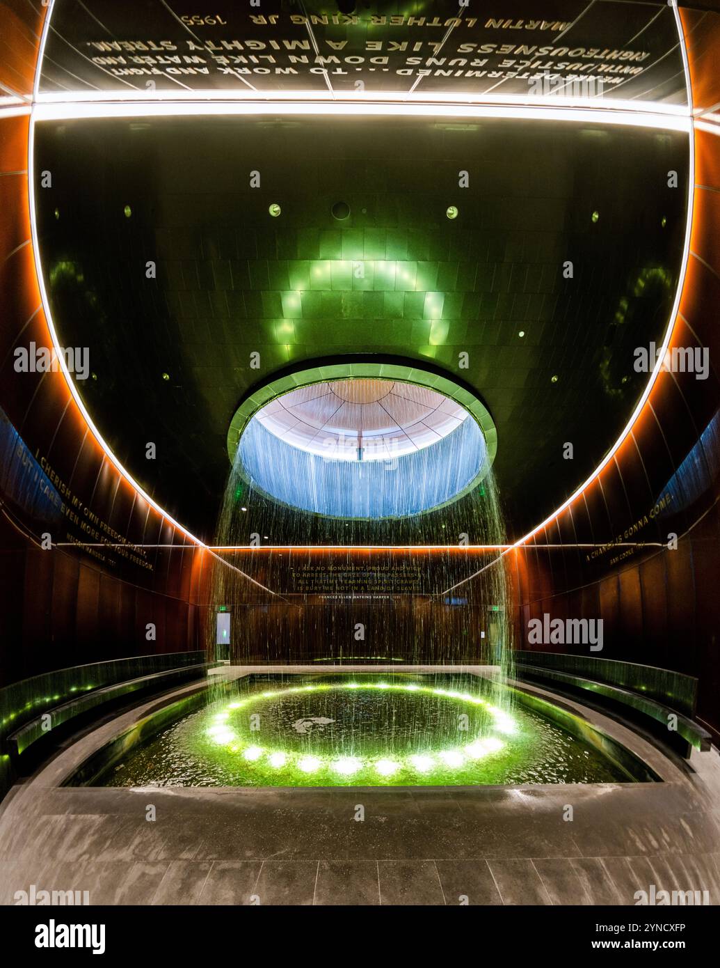 Fontaine de cour contemplative du Musée national d'histoire afro-américaine Washington DC // WASHINGTON DC — la cour contemplative du Musée national d'histoire et de culture afro-américaine présente une fontaine cylindrique tombant d'une lucarne dans une piscine centrale. Conçu par l'architecte Phil Freelon, l'espace comprend des murs en verre Bendheim en bronze caramel avec des noyaux de mailles lumineux. Cet espace de méditation offre aux visiteurs un lieu de réflexion après avoir vu les expositions du musée. Banque D'Images