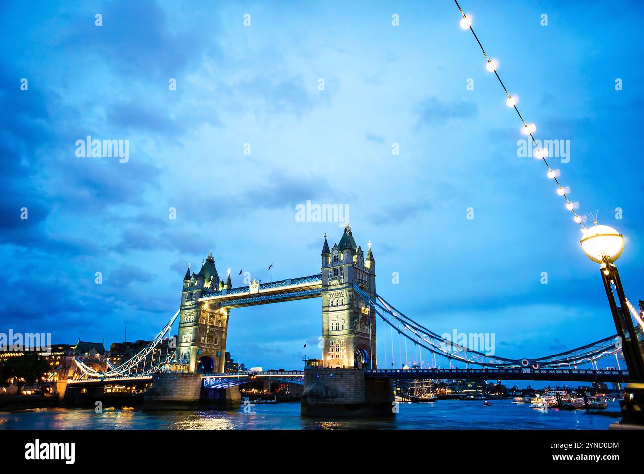Tower Bridge illuminé au crépuscule Londres Angleterre // LONDRES, Angleterre — Tower Bridge, l'emblématique pont victorien de Londres, illuminé au crépuscule sur la Tamise. La structure néo-gothique, achevée en 1894, combine des éléments de pont basculant et suspendu. L'éclairage du soir souligne les caractéristiques architecturales distinctives du pont et sa conception technique historique. Banque D'Images