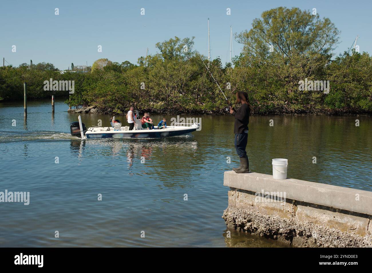 À côté d'une digue avec un pêcheur sur une jetée de pêche comme un bateau avec plusieurs personnes passe par. Vue sur l'eau jusqu'aux arbres verdoyants. À la sortie Marina Banque D'Images