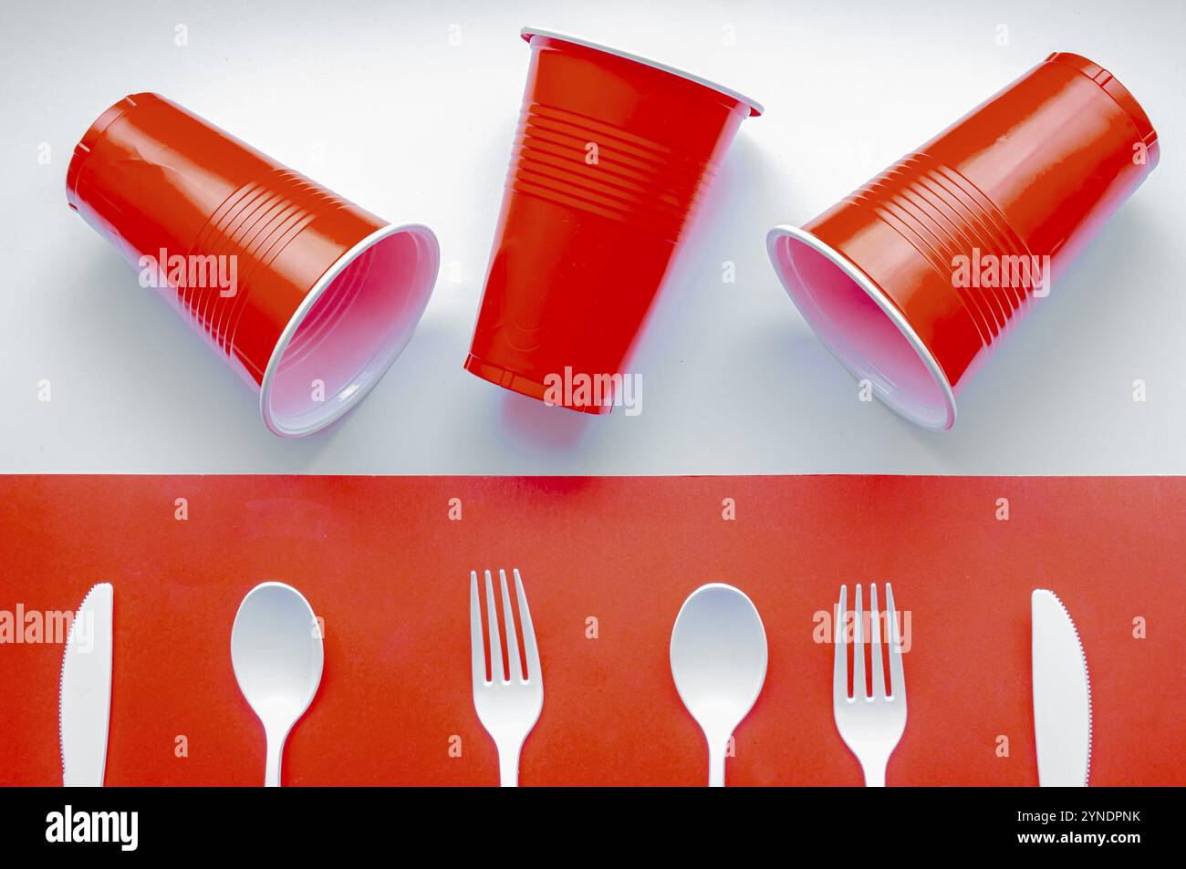 Couverts en plastique blanc à usage unique et verre en plastique rouge sur fond rouge et blanc. Concept : interdiction du plastique à usage unique Banque D'Images