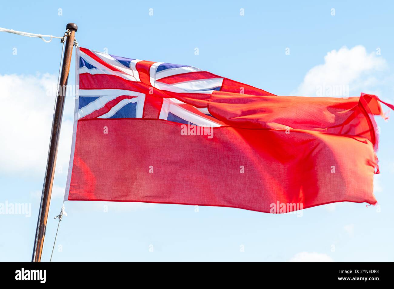 Un Red Ensign effiloché, ou drapeau Red Duster volant dans la brise contre un ciel bleu, Falmouth, Royaume-Uni Banque D'Images