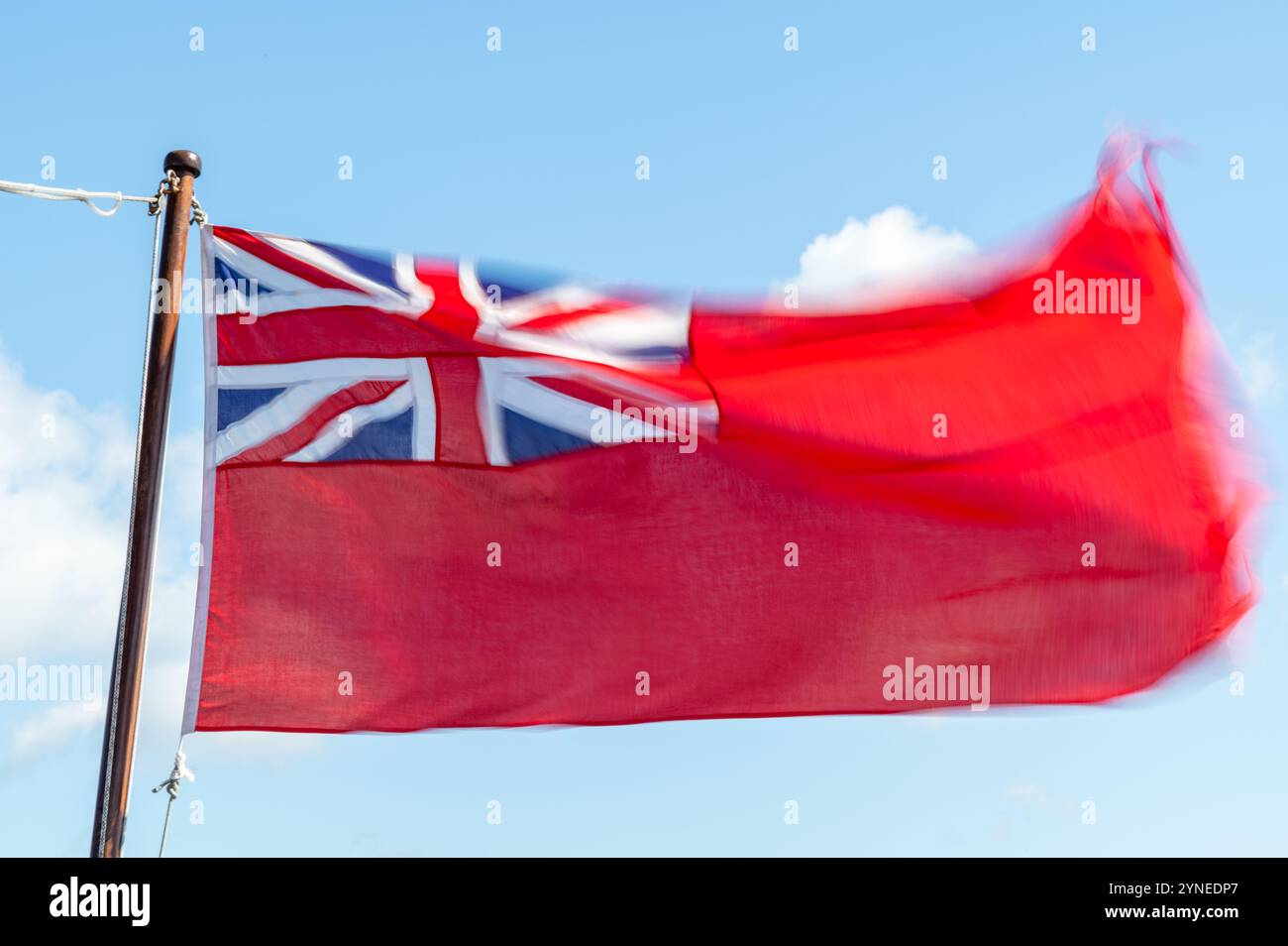 Un Red Ensign effiloché, ou drapeau Red Duster volant dans la brise contre un ciel bleu, Falmouth, Royaume-Uni Banque D'Images