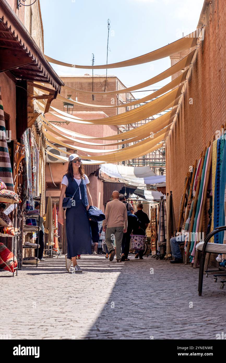 Jeune femme aux cheveux foncés en costume bleu marine et chapeau blanc debout dans une rue couverte à Marrakech, Maroc Banque D'Images