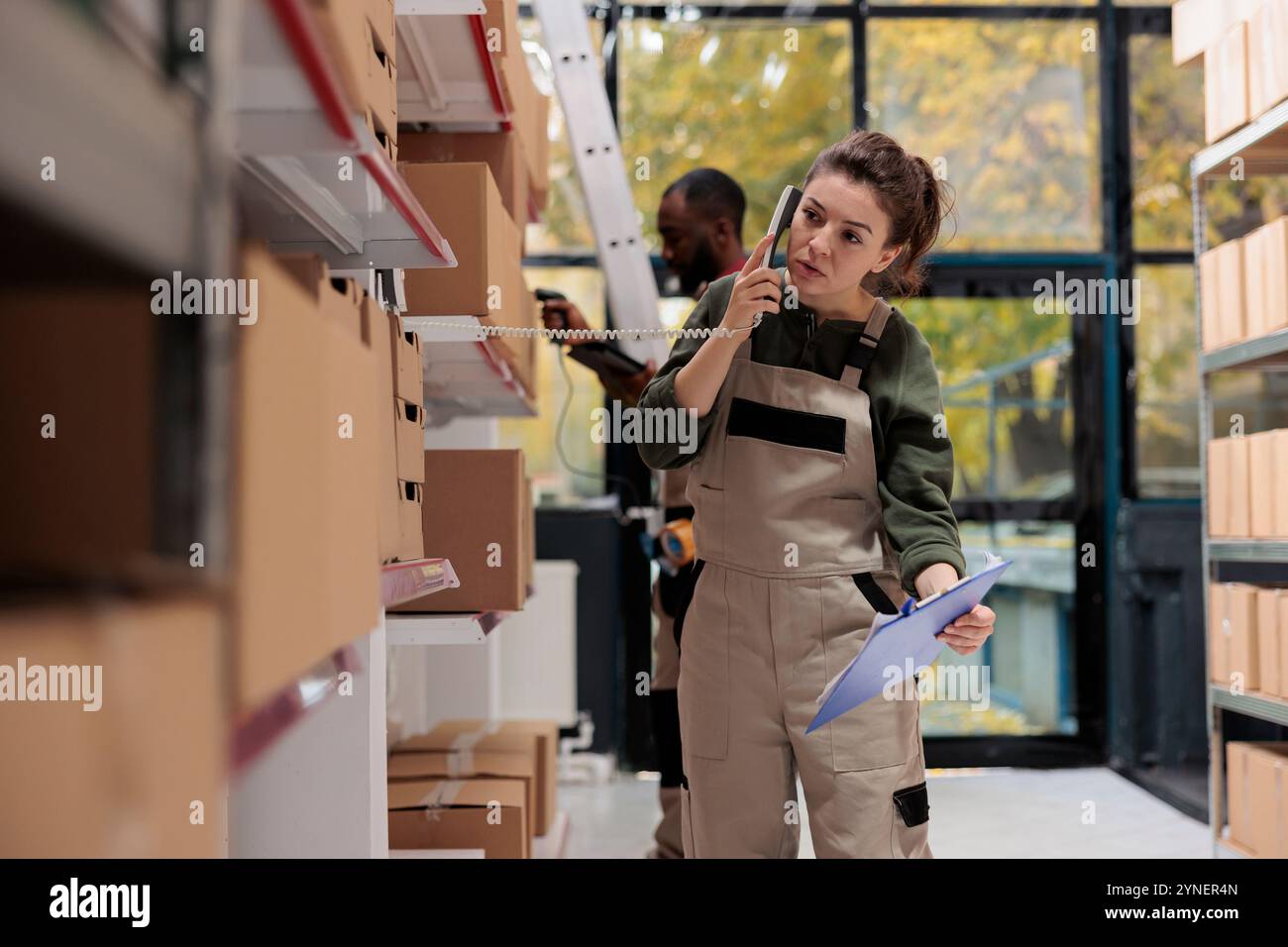 Femme superviseur parlant au téléphone fixe avec le gestionnaire à distance, discutant de l'inventaire des produits dans l'entrepôt. Employé travaillant aux commandes des clients, préparant des boîtes en carton pour l'expédition Banque D'Images
