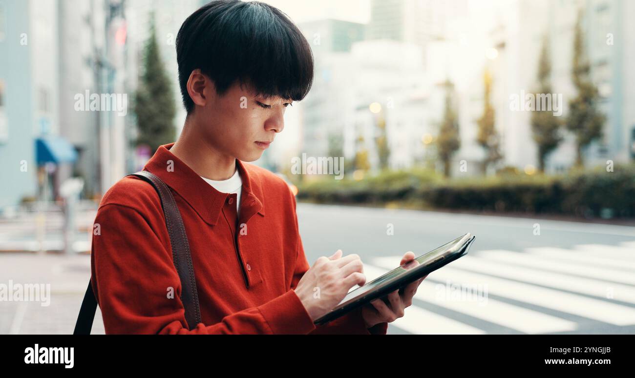 Ville, défilement et homme dans la rue avec tablette, trajet matinal ou recherche de navigation routière sur le passage à pied. Étudiant en milieu urbain, voyage et université japonaise sur Banque D'Images
