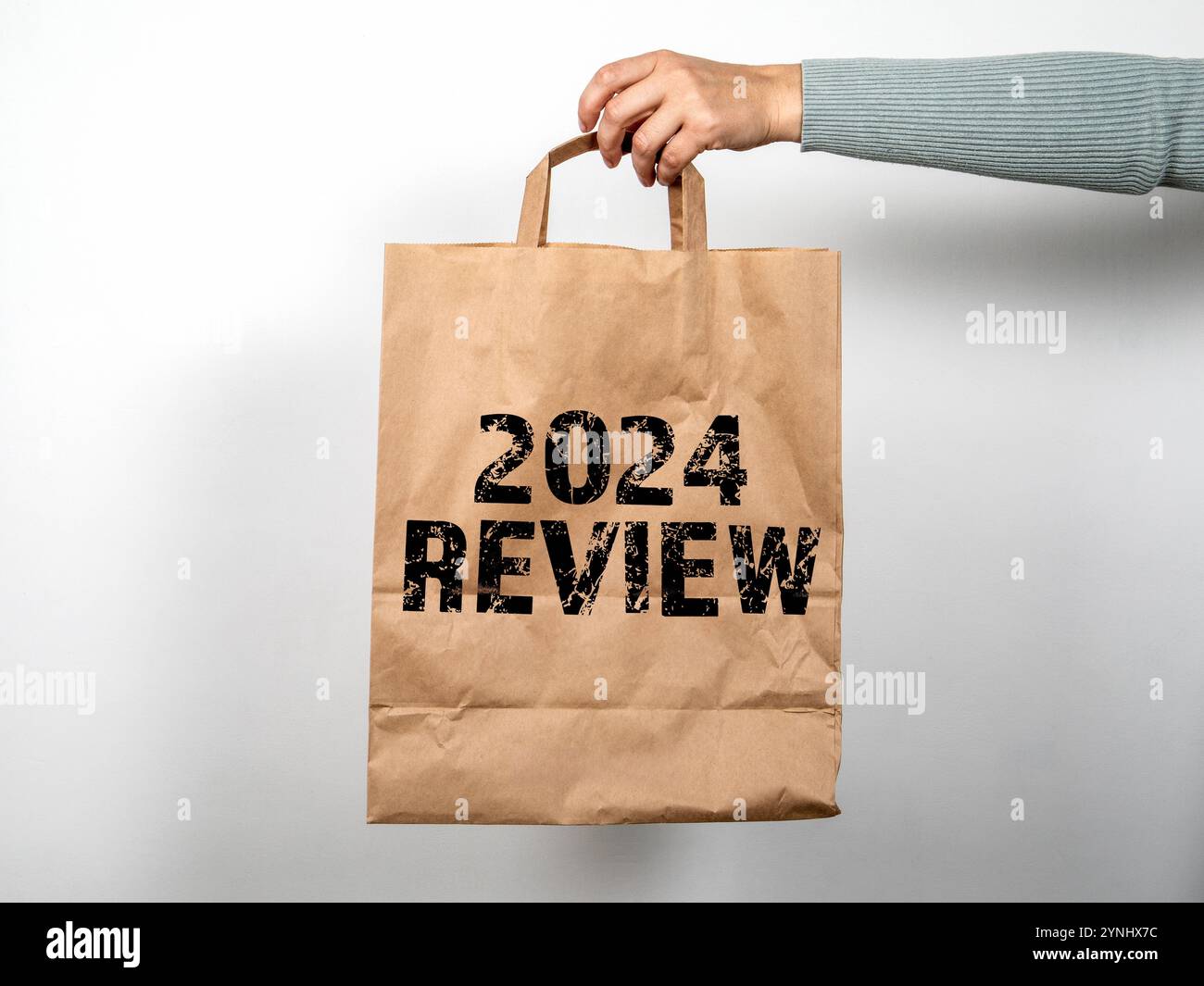 révision de 2024. En main un sac à provisions en papier sur un fond blanc. Banque D'Images