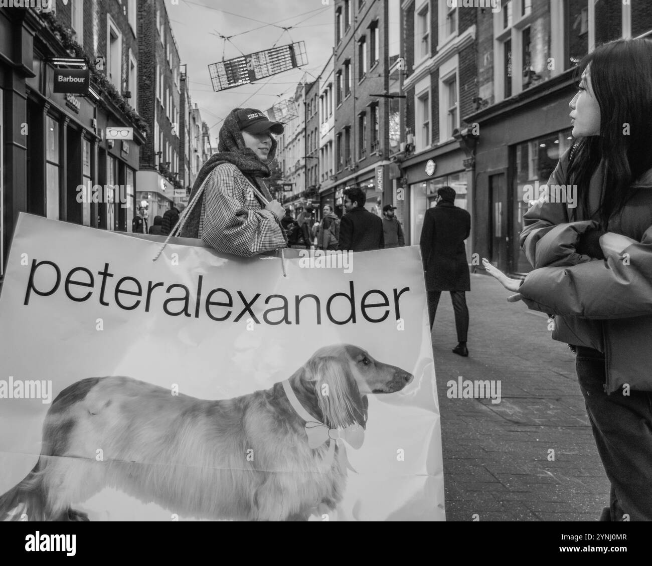 Image en noir et blanc d'un client transportant un sac géant Peter Alexander sur Carnaby Street à Londres. Banque D'Images
