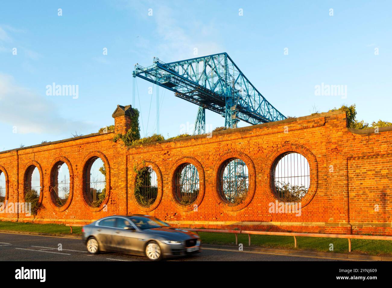 Vitesse de voiture devant le vieux mur de briques rouges vulcan Salt fonctionne avec des ouvertures circulaires et pont de transporteur bleu désutilisé en arrière-plan middlesbrough Teesside uk Banque D'Images