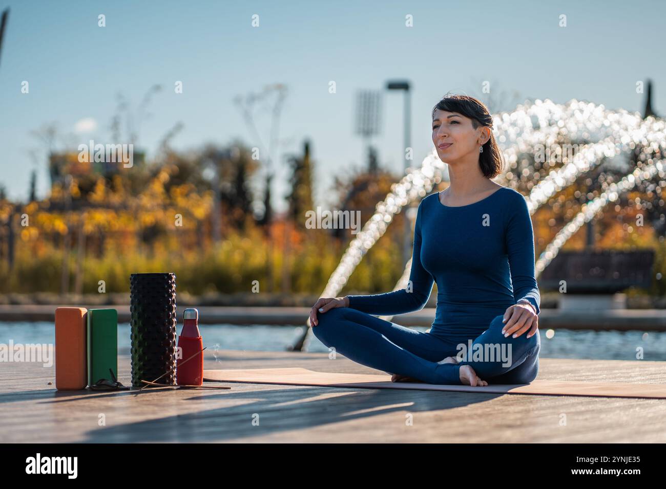 jeune belle femme pratiquant le yoga et méditant au coucher du soleil à l'extérieur, personne consciente du corps avec rouleau en mousse, blocs et bâtons indiens parfumés Banque D'Images