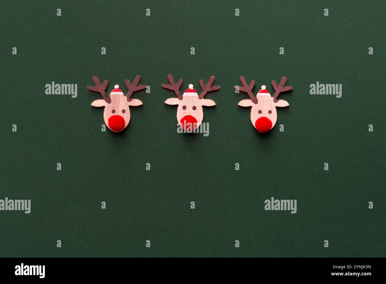 Trois rennes en bois faits à la main avec des nez en laine rouge sur un fond vert. Carte de Noël. Copier l'espace. Fond de Noël Banque D'Images