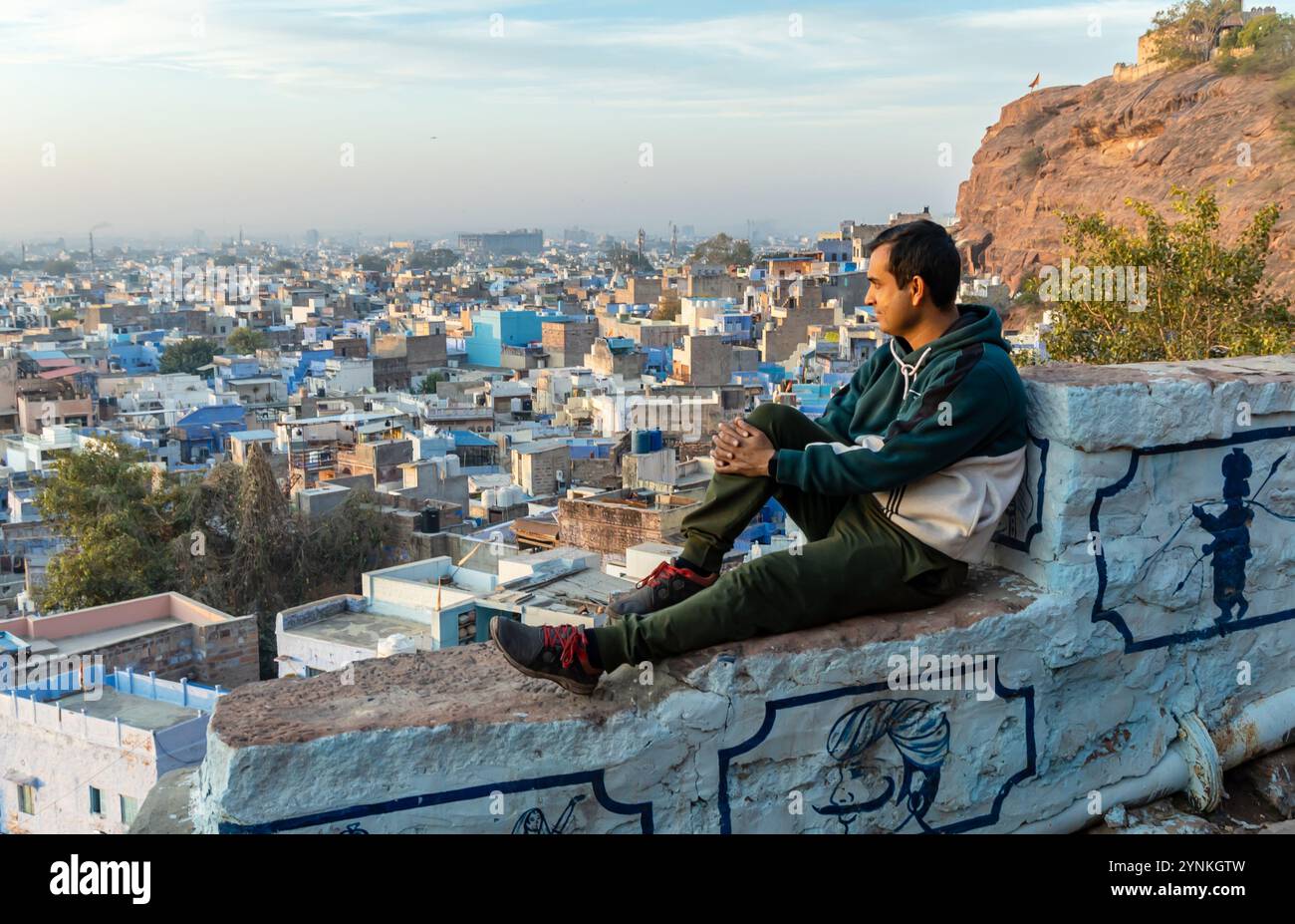 jeune homme assis au mur du fort et regardant la vue de la ville bondée du sommet de la montagne le matin Banque D'Images