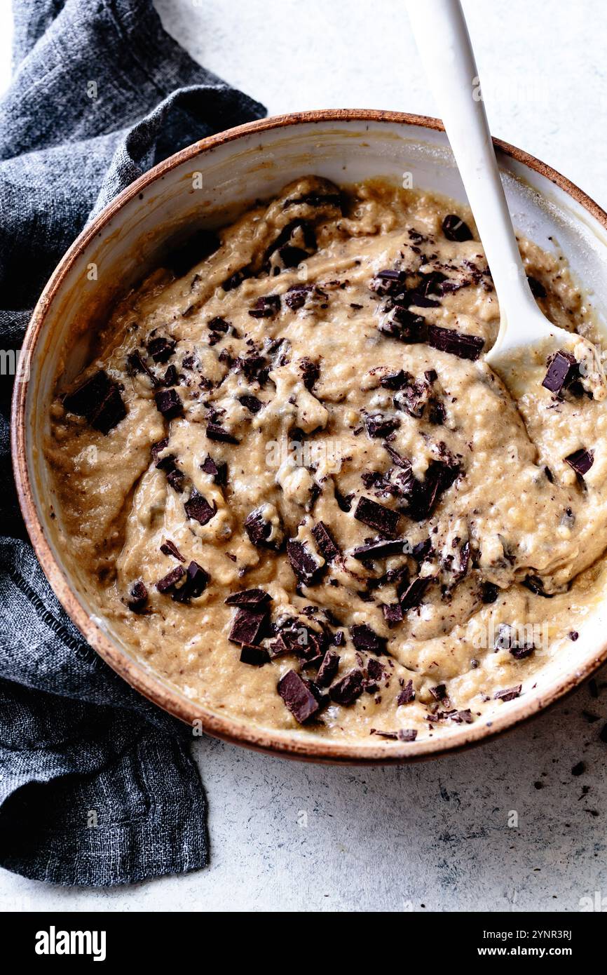 Un bol de pâte à biscuits avec des morceaux de chocolat noir mélangés, entouré d'un torchon gris. Banque D'Images
