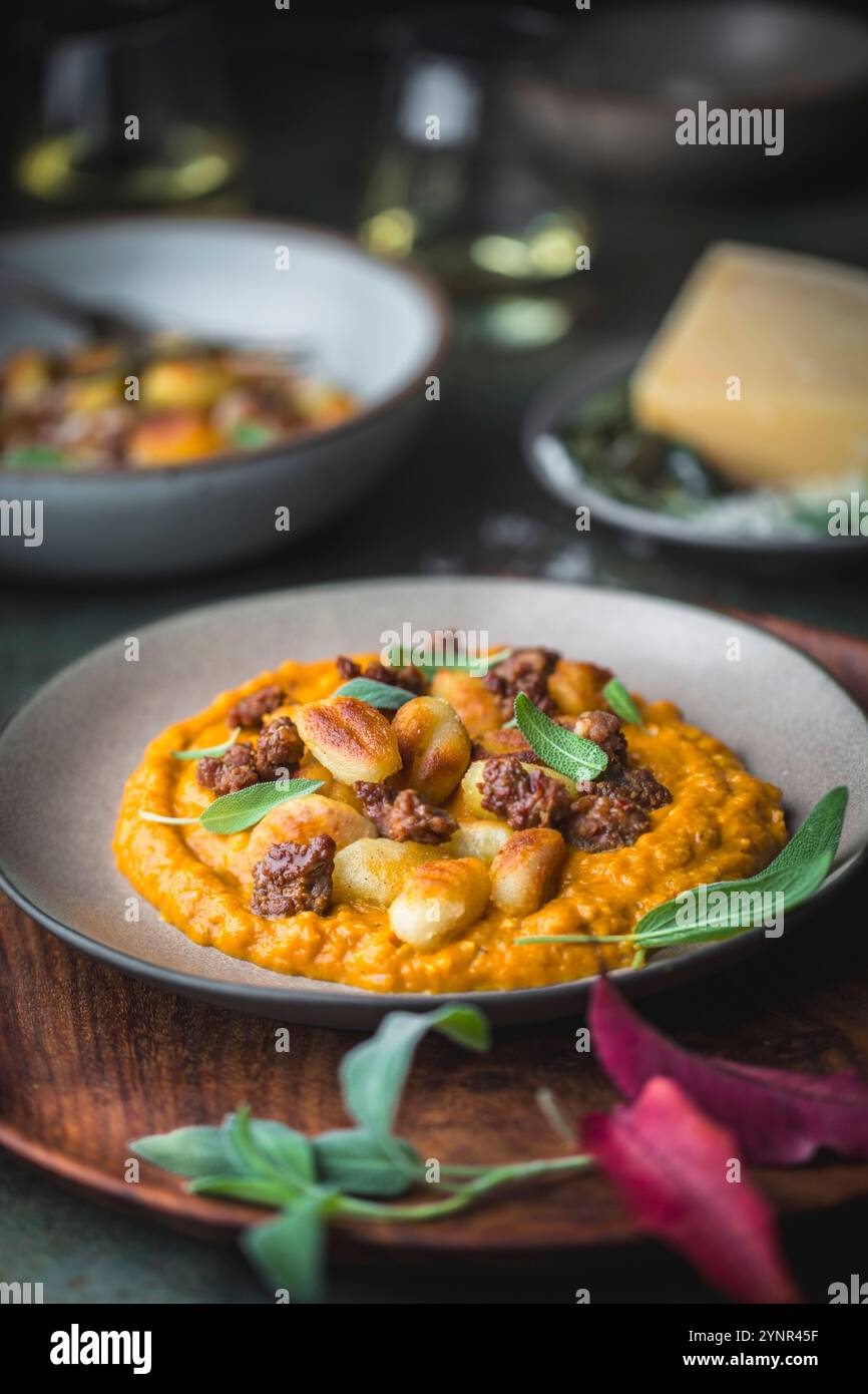Un plan latéral d'une assiette de gnocchi et saucisse avec de la sauge sur une sauce à la citrouille. Deux verres de vin blanc à l'arrière-plan iin un t automnal rustique Banque D'Images