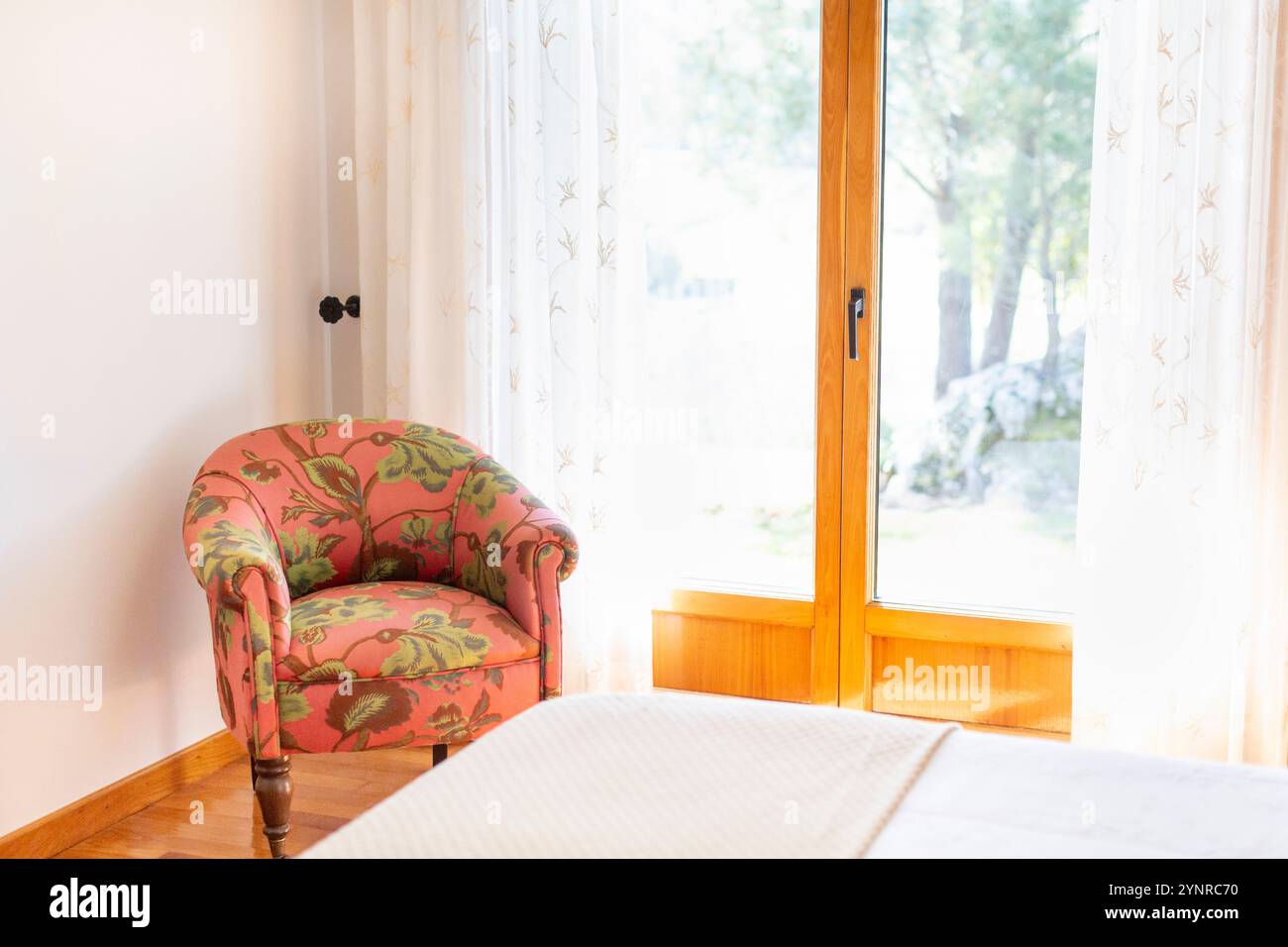 Porte double vitrage en bois naturel dans une chambre avec chaise basse tapissée de fleurs vertes en tissu couleur saumon, parquet naturel, cur blanc Banque D'Images