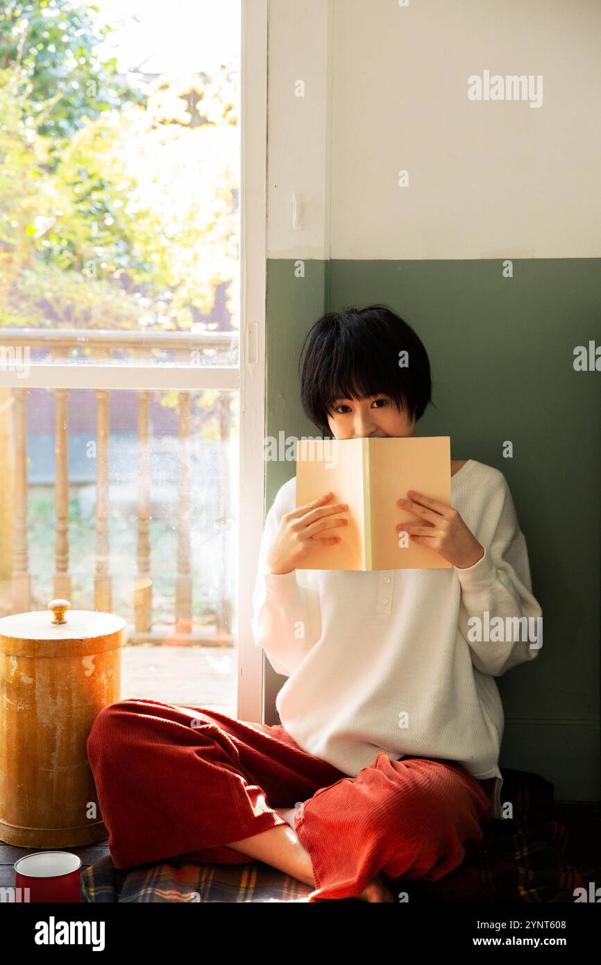 Femme dans la vingtaine tenant un livre et cachant son visage Banque D'Images