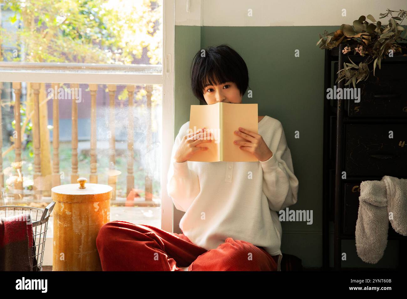 Femme dans la vingtaine tenant un livre et cachant son visage Banque D'Images