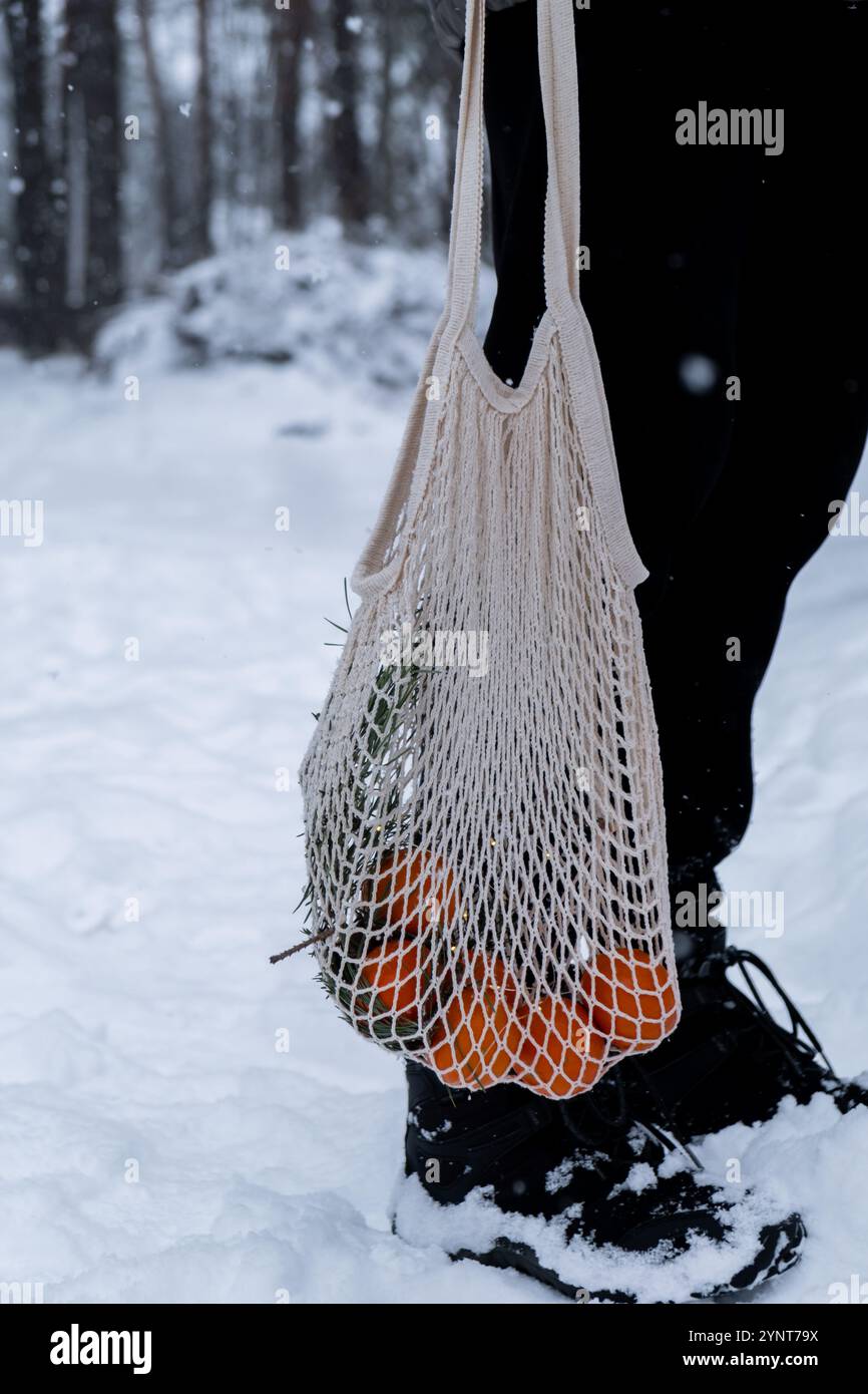 Mandarines mûres dans un sac en maille réutilisable à l'extérieur dans la forêt hivernale enneigée. Concept de célébration durable de Noël, de responsabilité et d'inclusivité. Oranges dans un sac en coton Banque D'Images