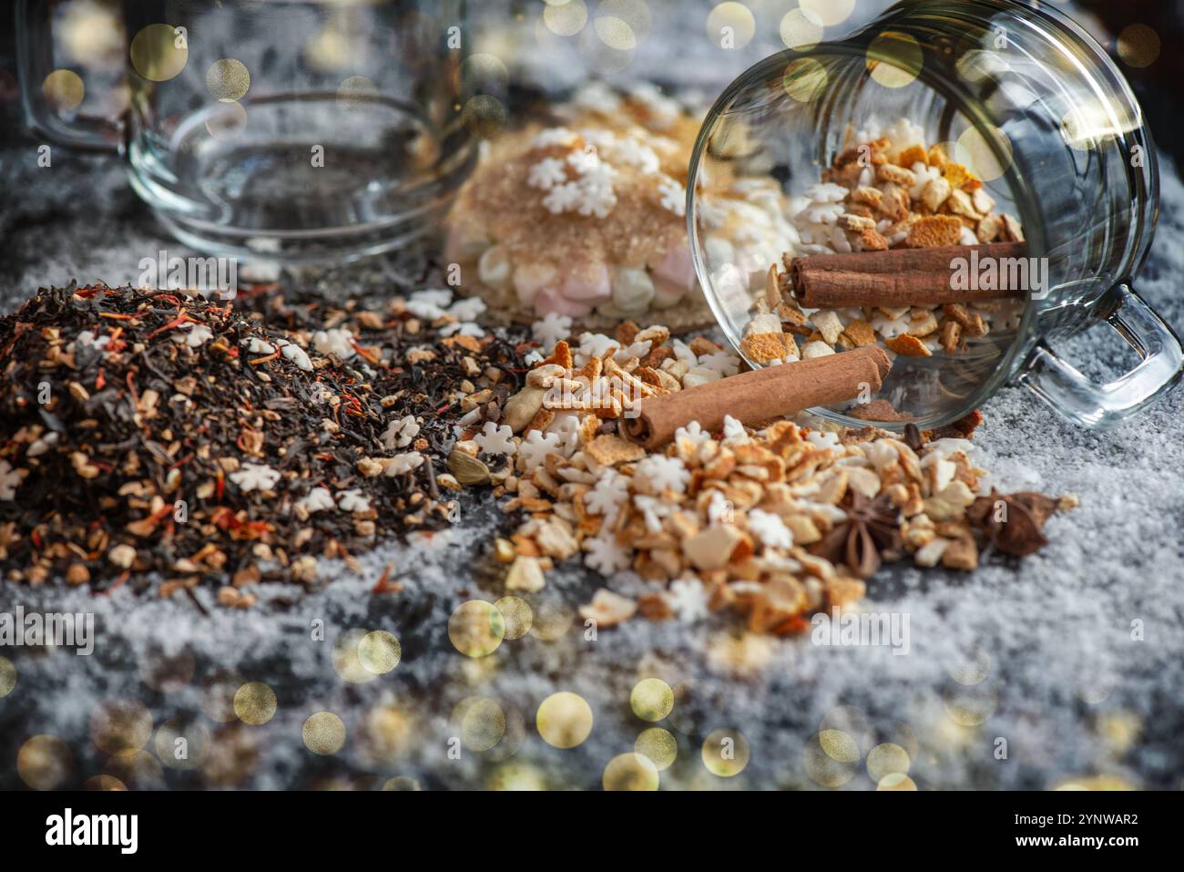 ingrédient de boisson chaude d'hiver renversé avec des épices, sucre en forme d'étoile et tasse de verre retournent sur fond neigeux et lumières de flou doré Banque D'Images