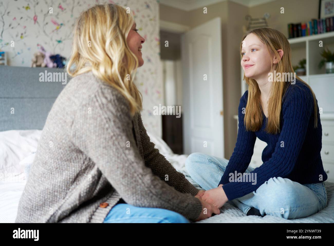 Mère mature assise sur le lit avec fille adolescente à la maison portant parler et rire ensemble Banque D'Images