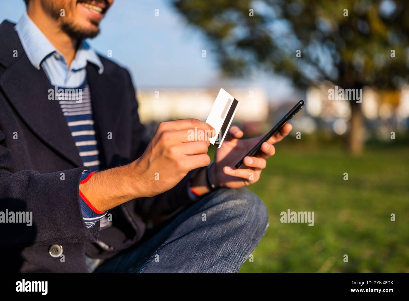 Gros plan photo de l'homme d'affaires utilisant le téléphone portable et la carte de crédit tout en étant assis sur le banc dans le parc. Banque D'Images