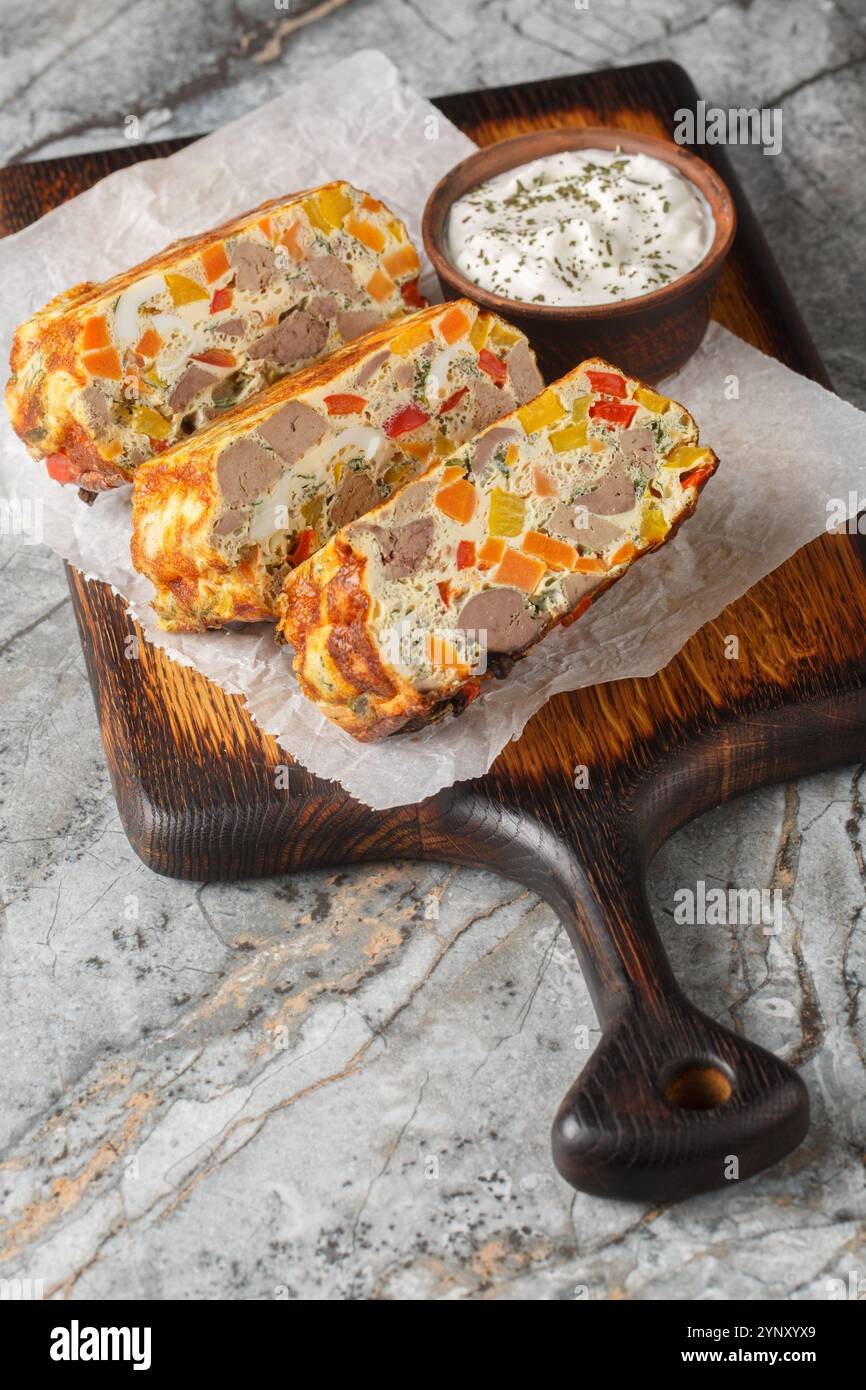 Cocotte de foie de poulet avec carottes, poivrons, herbes et œufs gros plan sur une planche de bois sur la table. Vertical Banque D'Images