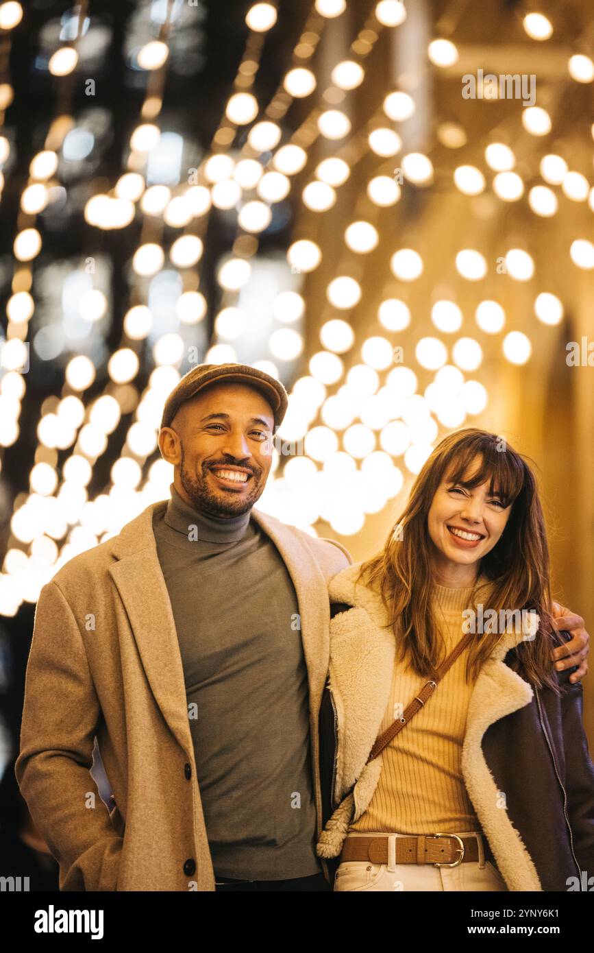 Un couple joyeux aime faire du shopping de Noël sous un auvent de lumières festives, embrassant l'esprit des fêtes ensemble. Banque D'Images