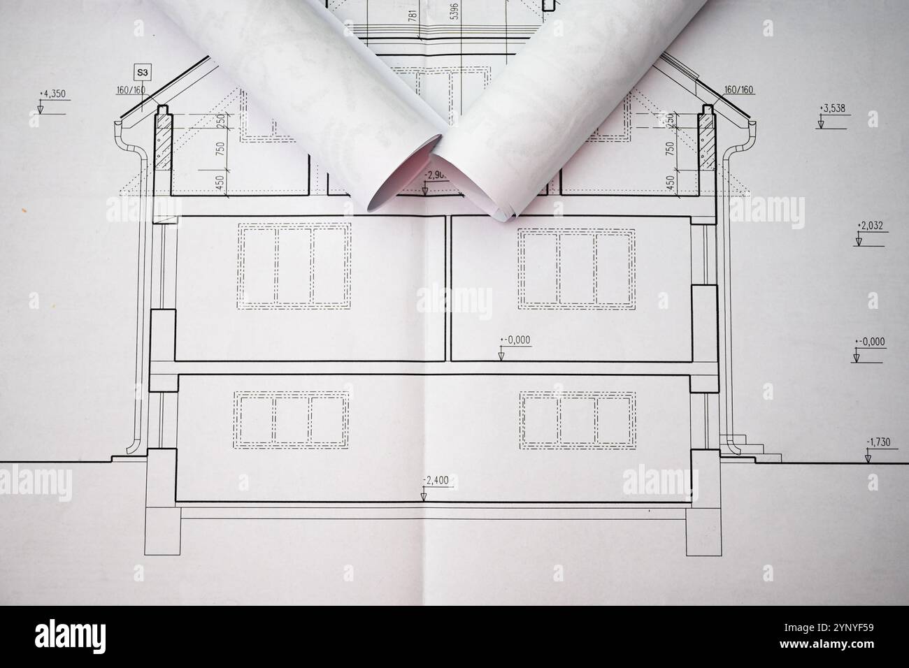 Les plans roulés reposent sur des plans de maison dépliés, mettant en valeur des mesures précises et des détails architecturaux. Banque D'Images