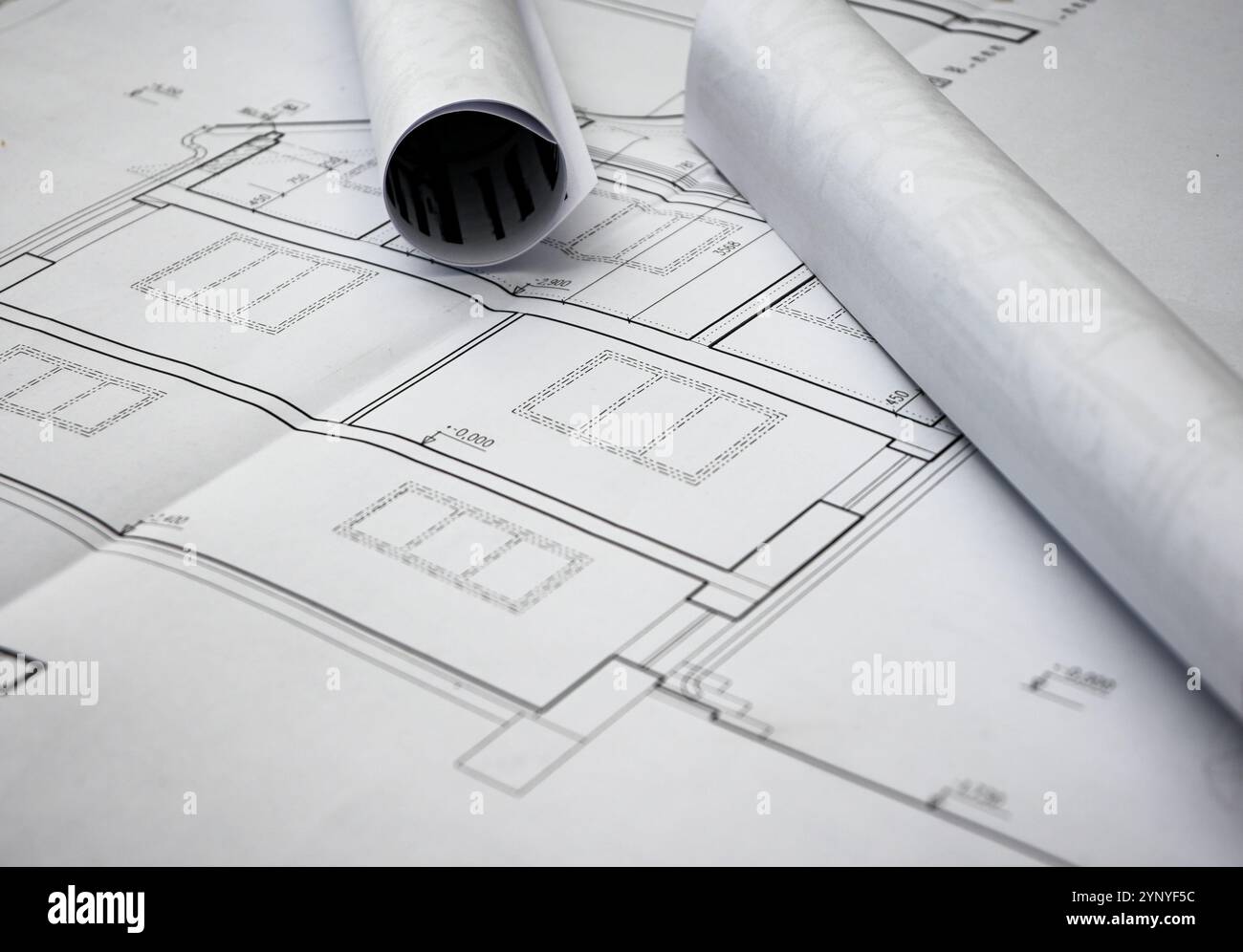 Les plans roulés reposent sur des plans de maison dépliés, mettant en valeur des mesures précises et des détails architecturaux. Banque D'Images