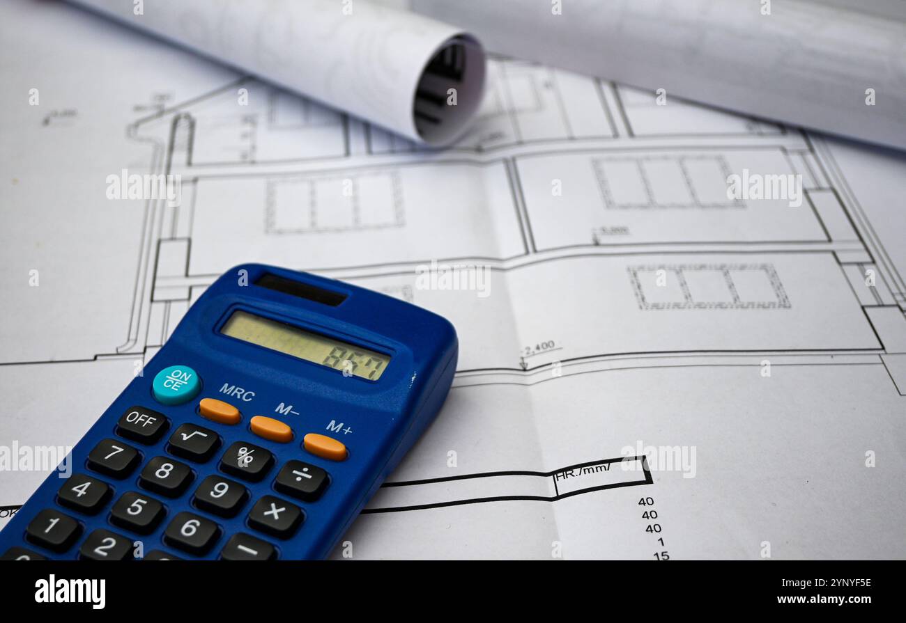 Calculatrice bleue placée au-dessus des plans roulés représentant la disposition de la maison, signifiant les coûts de construction et la budgétisation. Banque D'Images