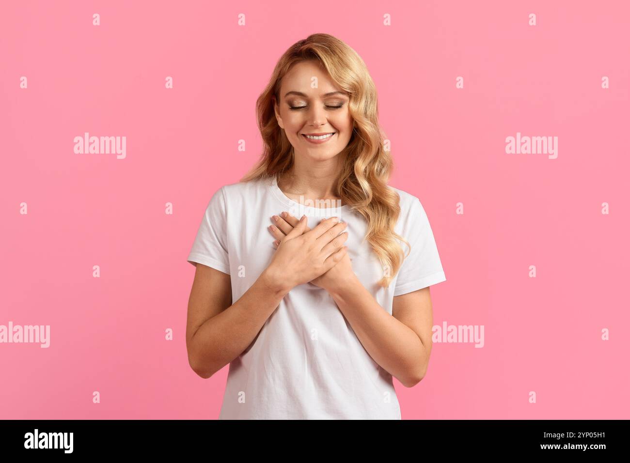 Jeune femme exprimant sa gratitude avec les mains sur le cœur sur fond rose Banque D'Images
