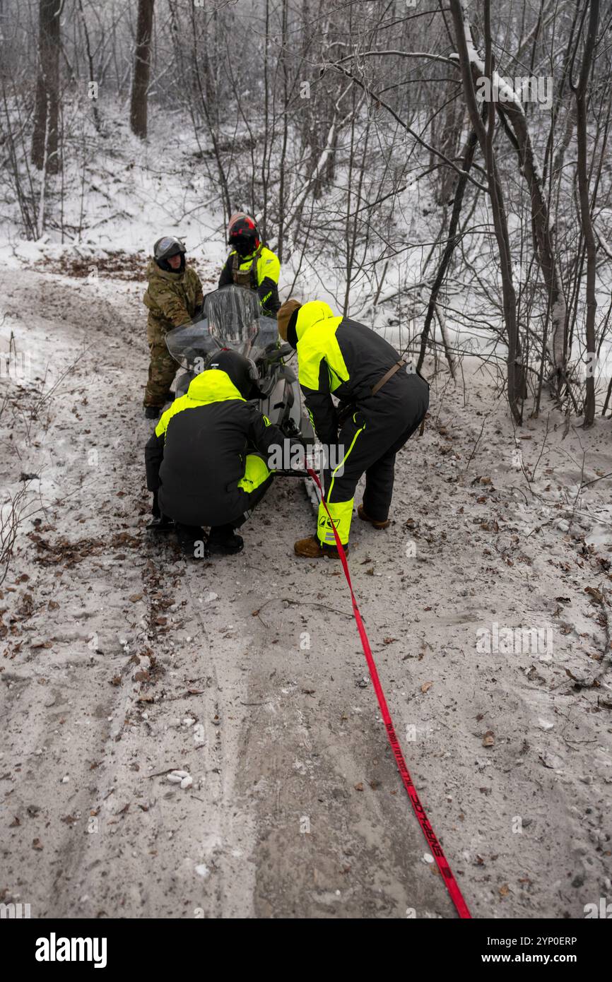 Les Marines des États-Unis avec le détachement d Company, le 4e bataillon d'application de la loi, le Groupe du quartier général de la Force, la réserve des Forces marines, et les aviateurs avec le 673e groupe médical, base interarmées Elemendorf-Richardson, attachent une sangle de remorquage à l'avant d'une motoneige lors d'une mission simulée de récupération de motoneige, Jim Creek, Alaska, 20 novembre 2024. Les techniciens de maintenance ont fixé la sangle de remorquage pendant qu'ils donnaient une formation sur la sécurité par temps froid afin de se préparer aux prochains événements Toys for Tots. La participation des Marines à cet entraînement les prépare à opérer dans des conditions météorologiques difficiles au-dessus du cercle arctique, leur permettant de se familiariser avec le Banque D'Images