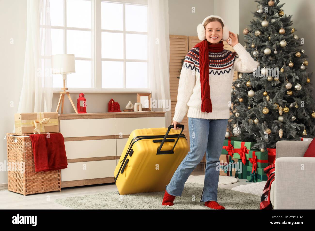 Voyageuse féminine avec des cache-oreilles et une valise à la maison le soir de Noël Banque D'Images