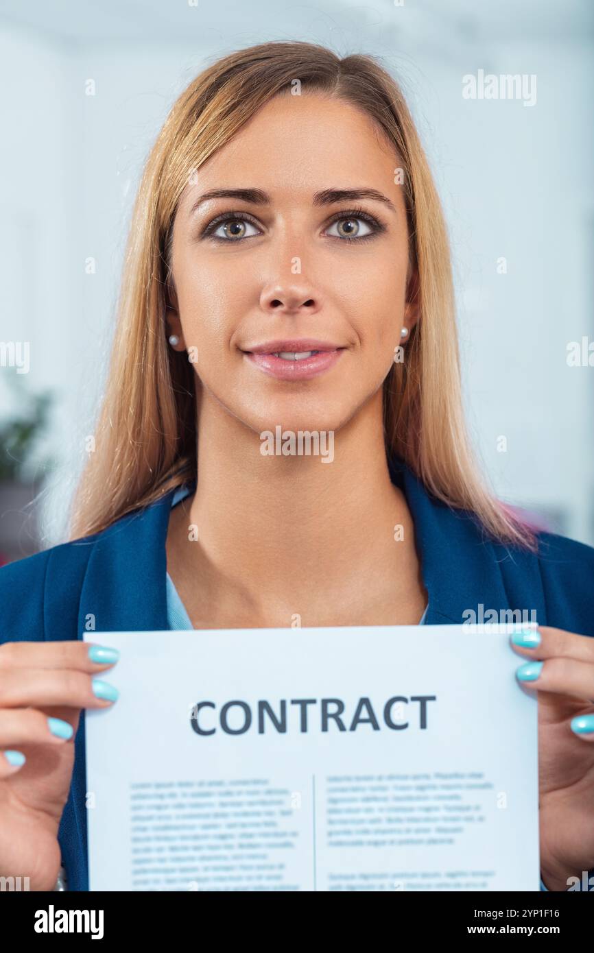 Jeune femme d'affaires confiante dans le bureau tenant le contrat, exsudant le succès et le professionnalisme, symbolisant le partenariat et le lien de carrière Banque D'Images