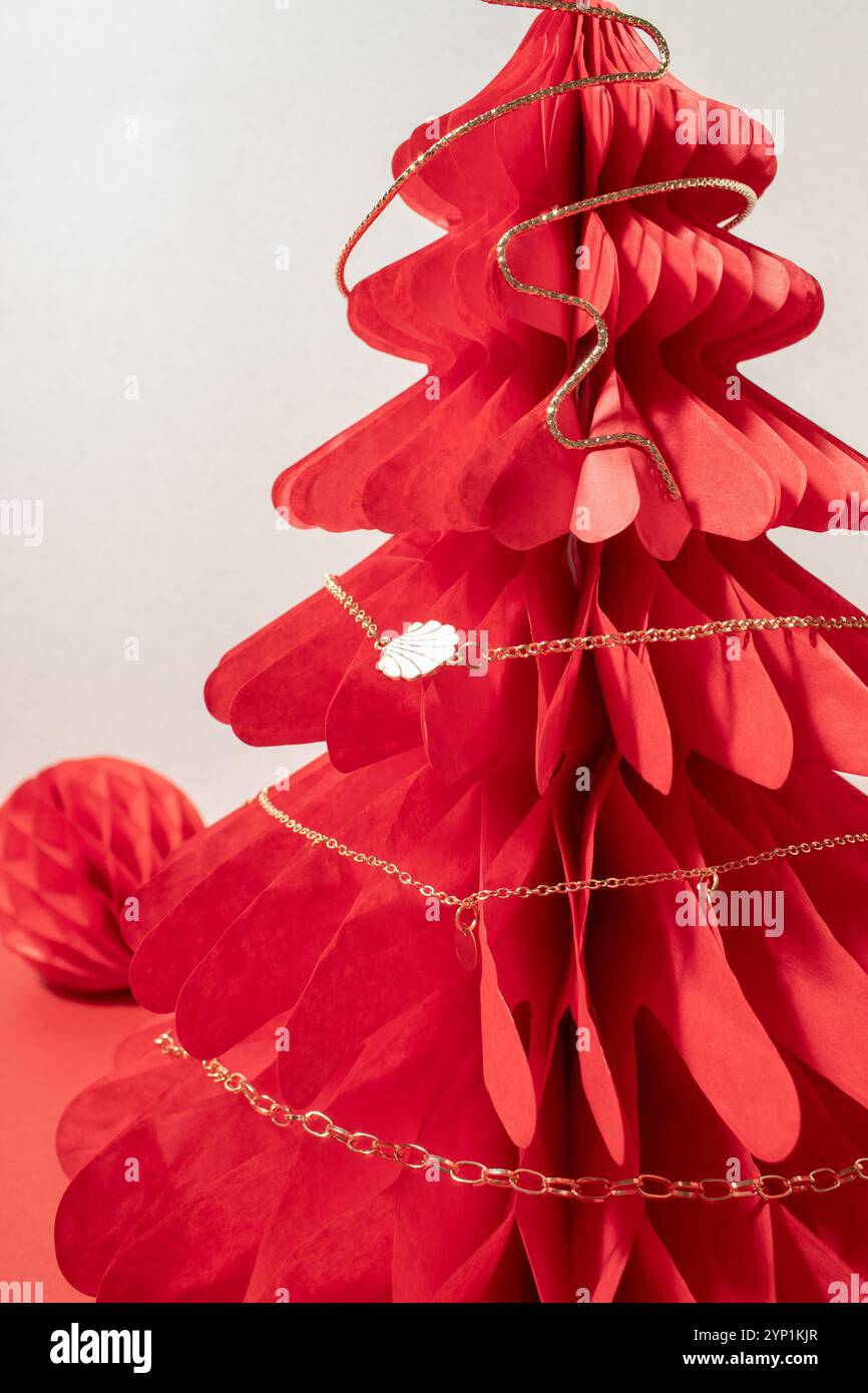 Collier de chane doré sur un arbre en nid d'abeille de Noël en papier rouge. Banque D'Images