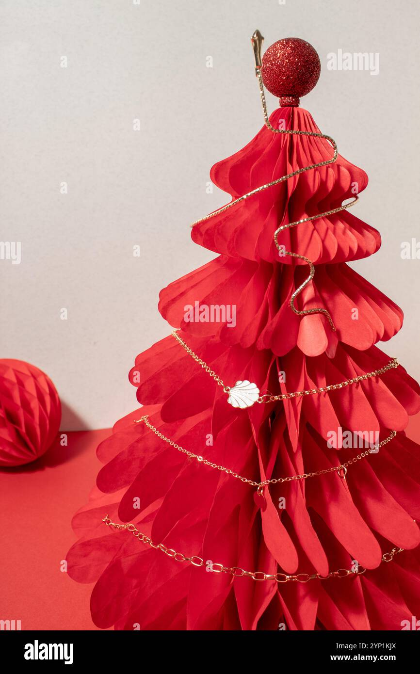 Collier de chane doré sur un arbre en nid d'abeille de Noël en papier rouge. Banque D'Images